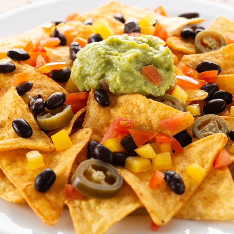 Close-up of nachos with guacamole, black beans, diced tomatoes, yellow peppers, and jalapeños.
